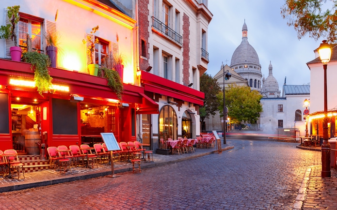 Montmartre street with Sacré-Cœur Basilica in Paris, featuring outdoor café seating.