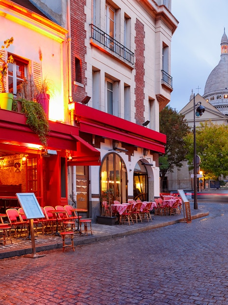 Montmartre street with Sacré-Cœur Basilica in Paris, featuring outdoor café seating.