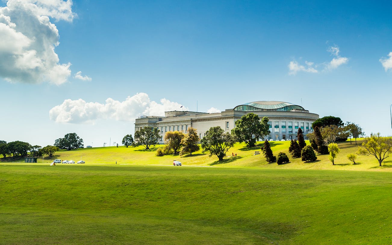 Auckland War Memorial Museum on a sunny day, surrounded by green lawns and trees.