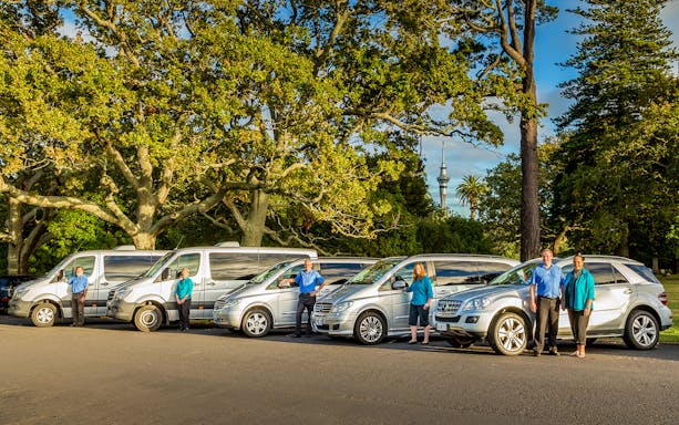 Tour vehicles parked under trees with Auckland's Sky Tower in the background.