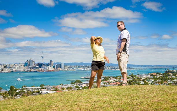 Tourists enjoying a view of Auckland skyline and Sky Tower from a hilltop.