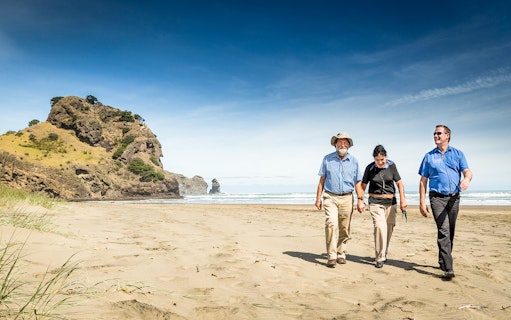 Group walking on Piha Beach, Auckland, with Lion Rock in the background.