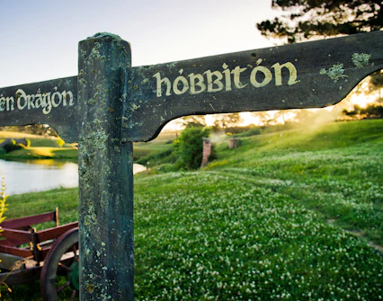 Signpost to Green Dragon and Hobbiton in lush landscape, part of Auckland to Waitomo Caves and Hobbiton tour.