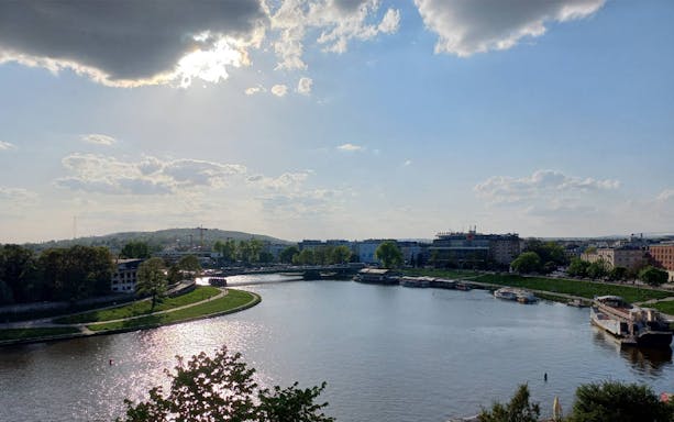 Vistula River view in Krakow with surrounding buildings and greenery.
