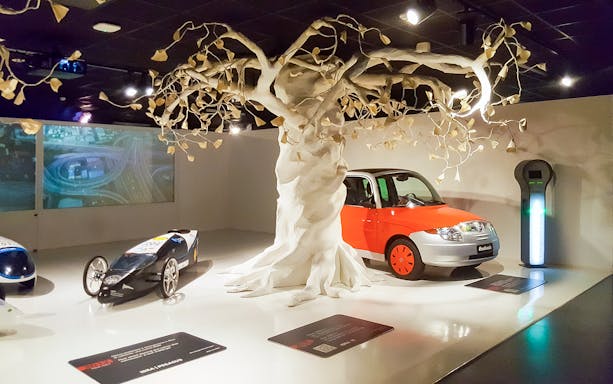 Car exhibit with futuristic vehicles and a sculpted tree at Torino Car Museum.