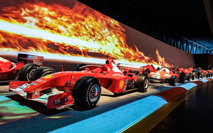 Formula 1 cars displayed at Torino Car Museum with fiery backdrop.