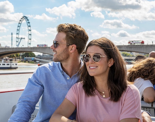 Couple enjoying a boat tour on the Thames with the London Eye in the background.
