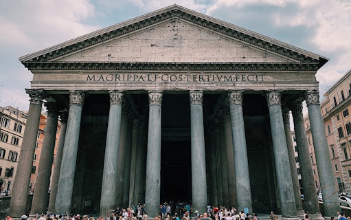 Pantheon facade in Rome with tourists gathered outside.