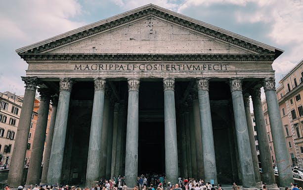 Pantheon facade in Rome with tourists gathered outside.