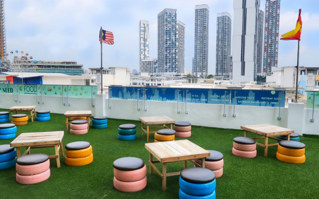 Rooftop seating area with colorful tire stools and tables, overlooking Shah Alam skyline.