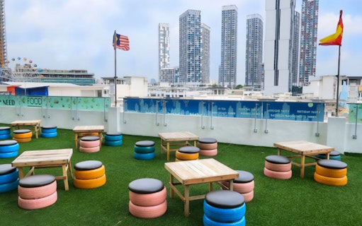 Rooftop seating area with colorful tire stools and tables, overlooking Shah Alam skyline.