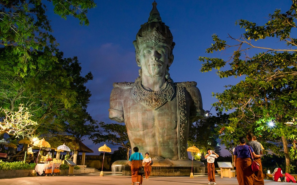 Garuda Wisnu Kencana statue at dusk in Bali's culture park, surrounded by visitors.