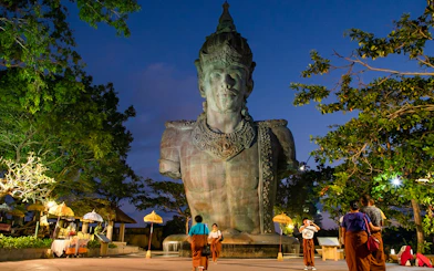 Garuda Wisnu Kencana statue at dusk in Bali's culture park, surrounded by visitors.