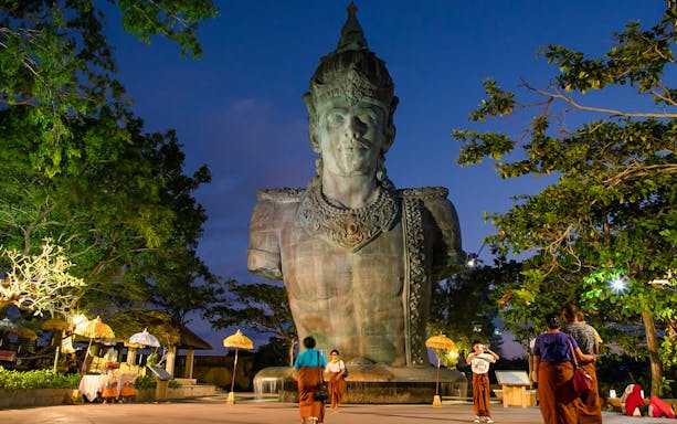 Garuda Wisnu Kencana statue at dusk in Bali's culture park, surrounded by visitors.