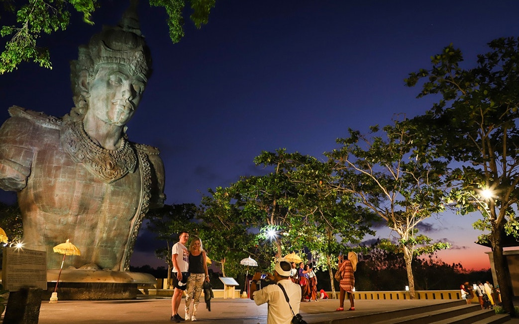 Visitors at Garuda Wisnu Kencana Culture Park in Bali at sunset, with the statue in view.