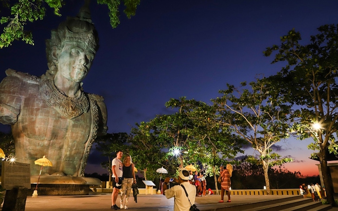 Visitors at Garuda Wisnu Kencana Culture Park in Bali at sunset, with the statue in view.