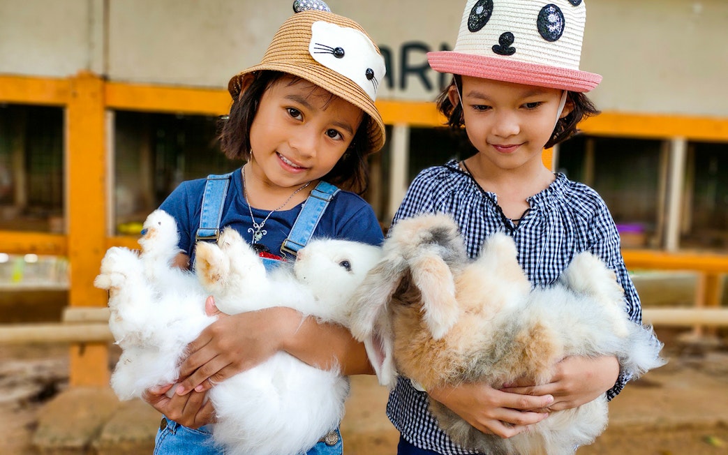 Children holding rabbits at Zoo Melaka petting area.