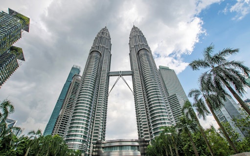 Petronas Twin Towers in Kuala Lumpur with surrounding skyscrapers and palm trees.