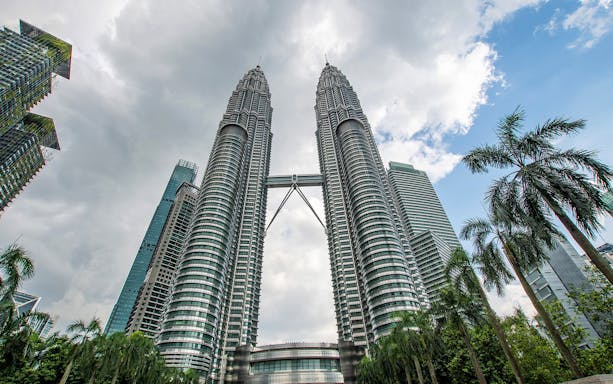 Petronas Twin Towers in Kuala Lumpur with surrounding skyscrapers and palm trees.