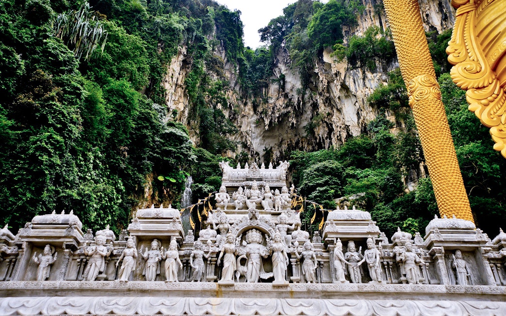 Batu Caves temple facade with intricate statues and lush limestone cliffs in Kuala Lumpur.