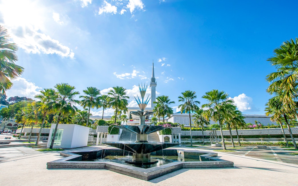 National Mosque of Kuala Lumpur with palm trees and fountain in foreground.