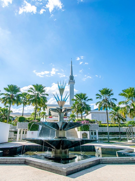National Mosque of Kuala Lumpur with palm trees and fountain in foreground.