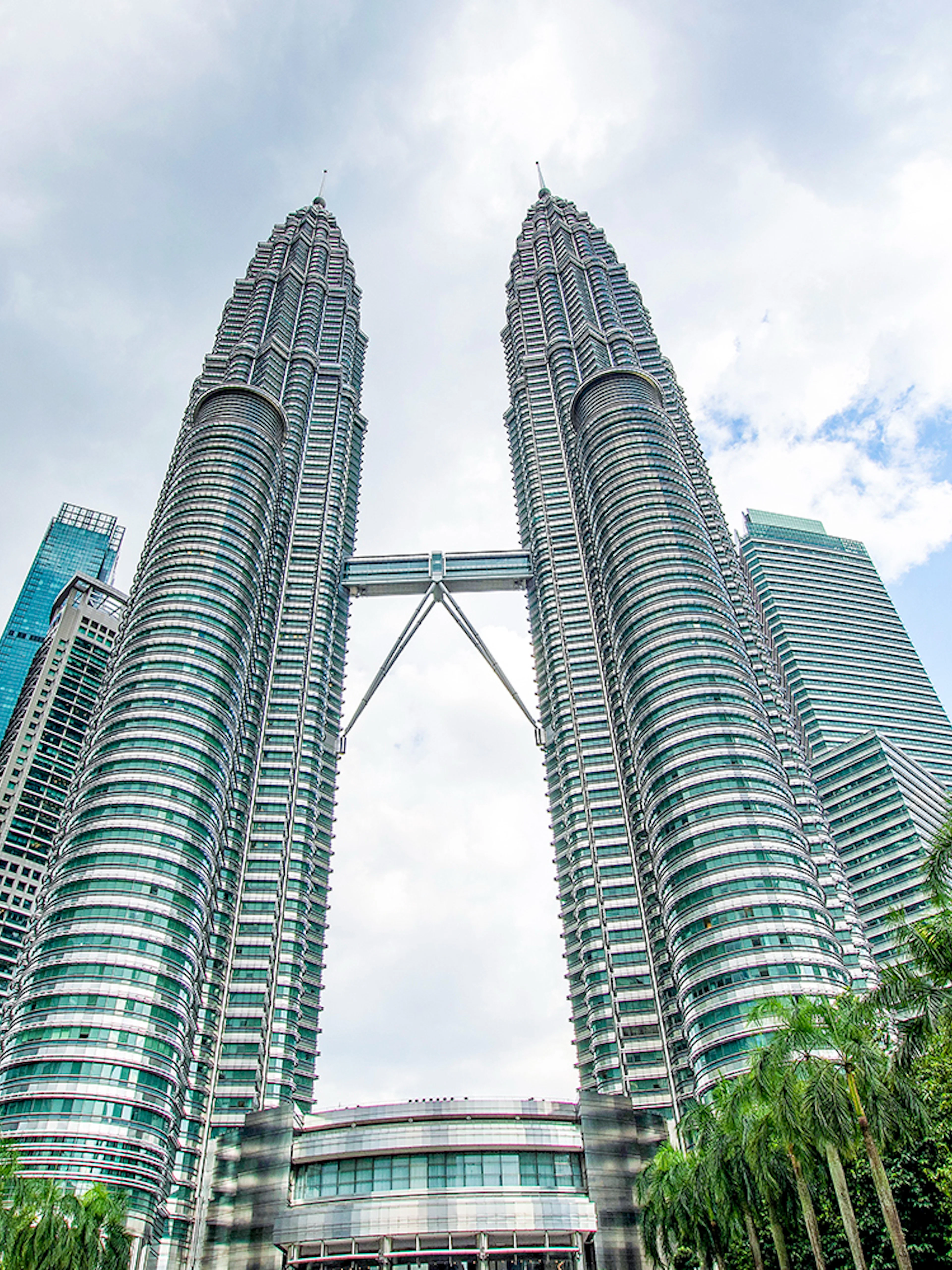 Petronas Twin Towers in Kuala Lumpur, Malaysia, viewed from below with surrounding skyscrapers.