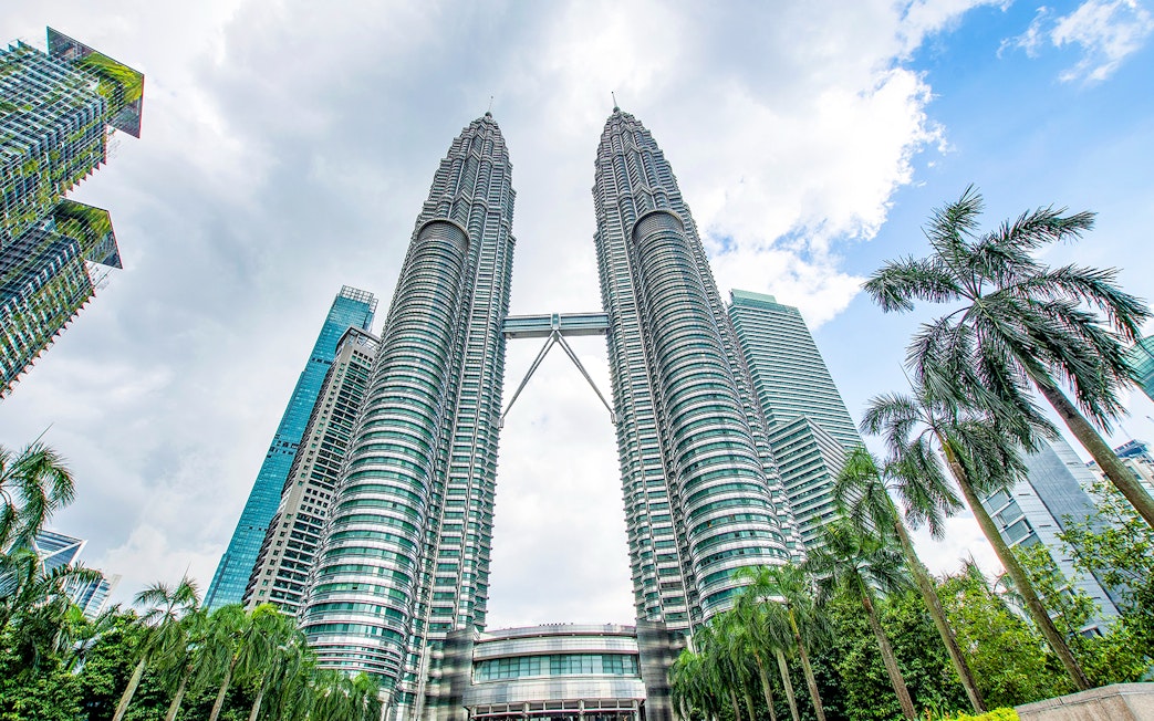 Petronas Twin Towers in Kuala Lumpur, Malaysia, viewed from below with surrounding skyscrapers.