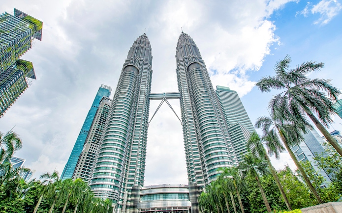 Petronas Twin Towers in Kuala Lumpur, Malaysia, viewed from below with surrounding skyscrapers.