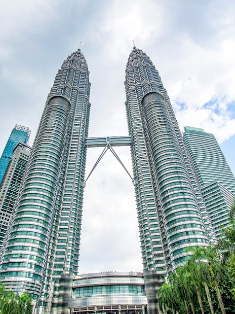 Petronas Twin Towers in Kuala Lumpur, Malaysia, viewed from below with surrounding skyscrapers.