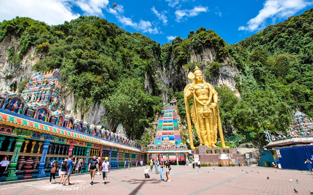 Golden statue of Lord Murugan at Batu Caves entrance, Kuala Lumpur, with colorful temple facade.