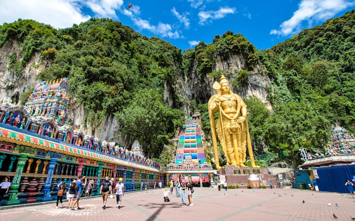 Golden statue of Lord Murugan at Batu Caves entrance, Kuala Lumpur, with colorful temple facade.