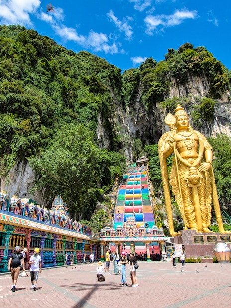 Golden statue of Lord Murugan at Batu Caves entrance, Kuala Lumpur, with colorful temple facade.