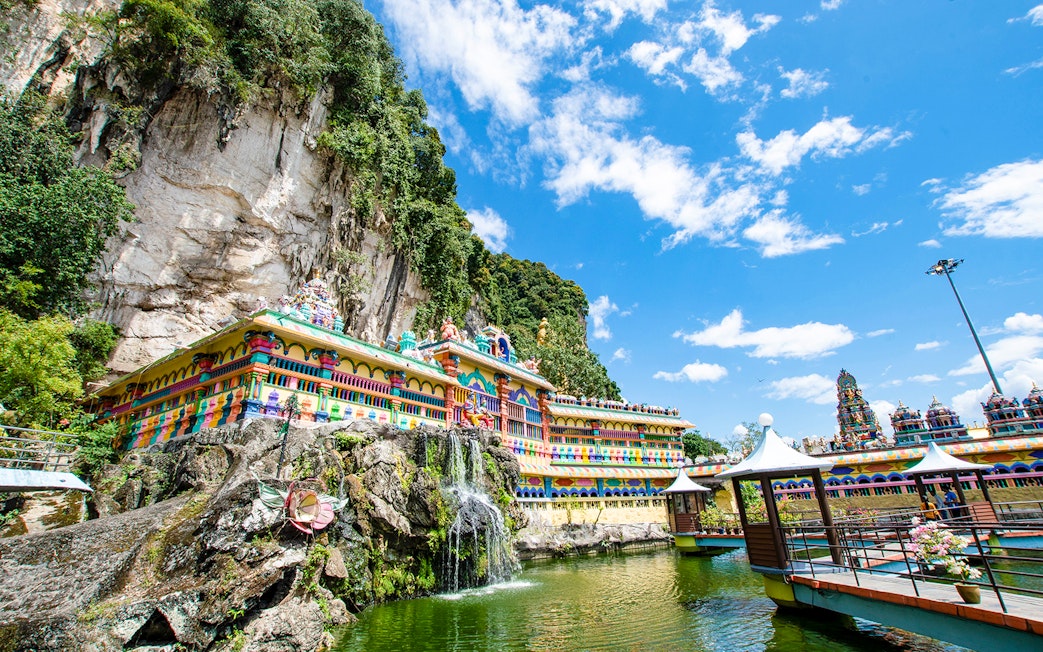 Colorful temple facade at Batu Caves, Kuala Lumpur, with limestone cliffs and blue sky.