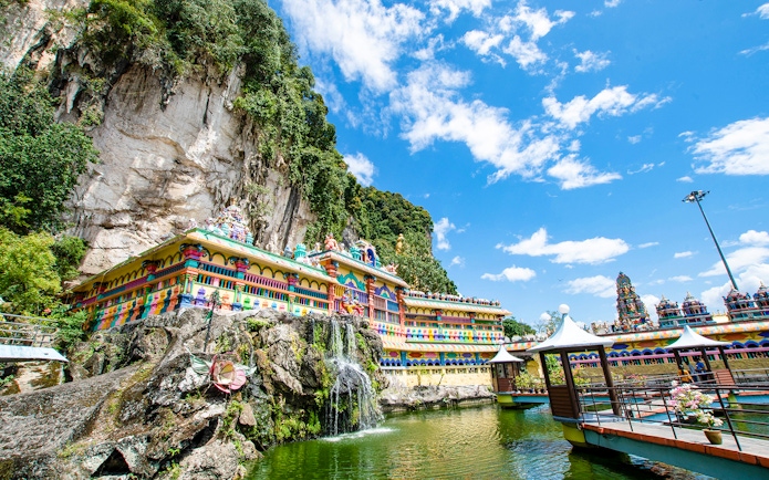 Colorful temple facade at Batu Caves, Kuala Lumpur, with limestone cliffs and blue sky.