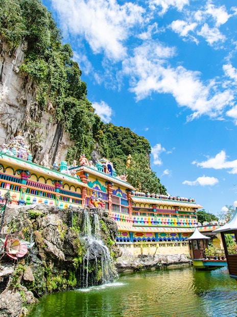 Colorful temple facade at Batu Caves, Kuala Lumpur, with limestone cliffs and blue sky.