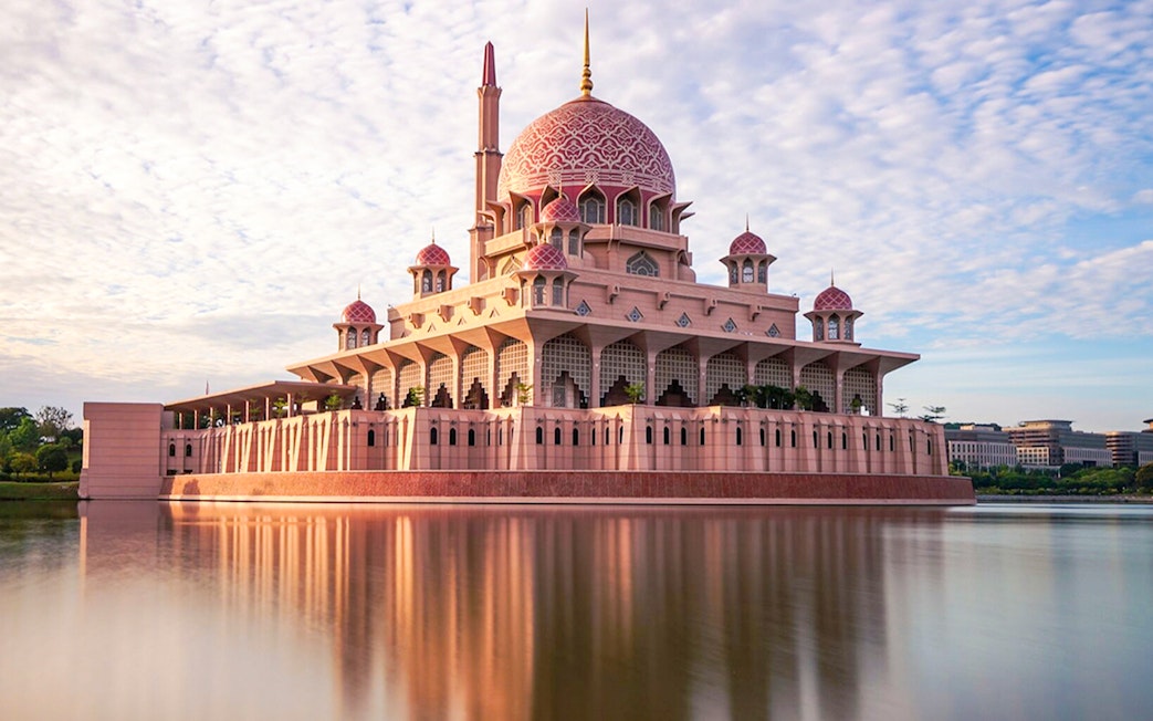 Putra Mosque reflecting in a lake under a blue sky in Kuala Lumpur.