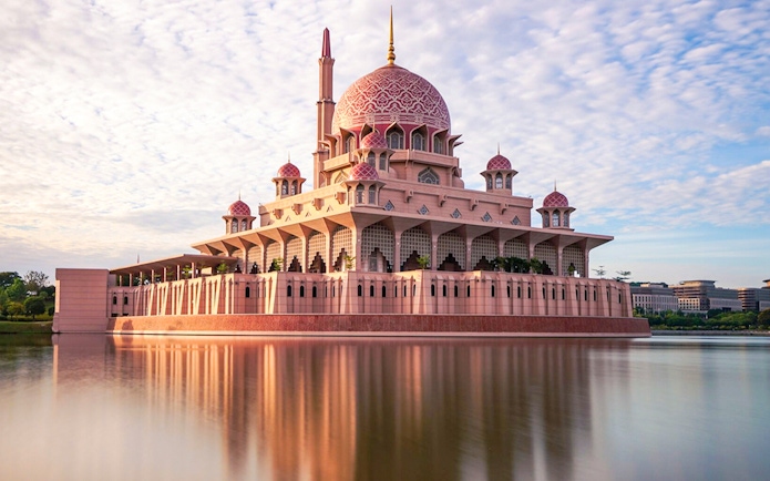Putra Mosque reflecting in a lake under a blue sky in Kuala Lumpur.