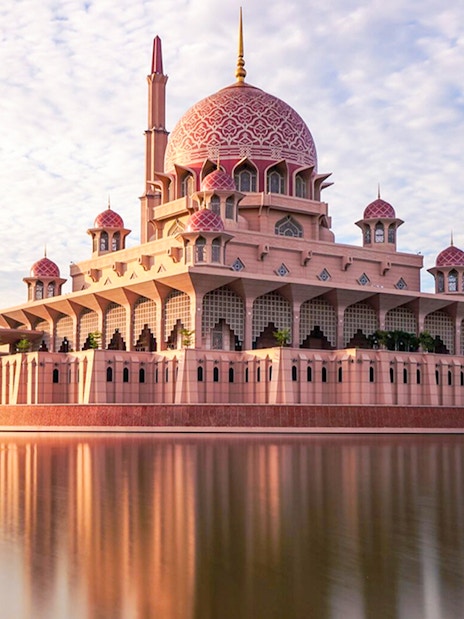 Putra Mosque reflecting in a lake under a blue sky in Kuala Lumpur.