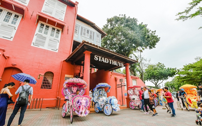 Stadthuys building in Melaka with colorful trishaws parked in front.
