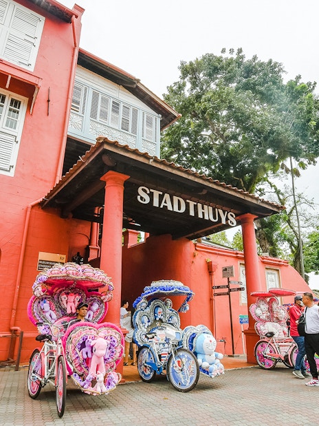 Stadthuys building in Melaka with colorful trishaws parked in front.