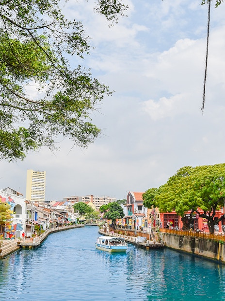 Melaka River with colorful buildings and a boat, part of the Historical Melaka Tour from Kuala Lumpur.