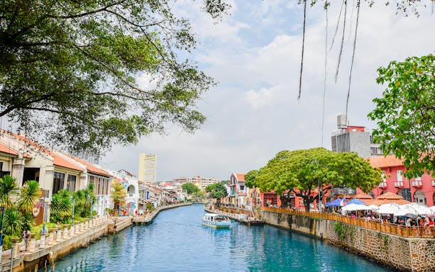 Melaka River with colorful buildings and a boat, part of the Historical Melaka Tour from Kuala Lumpur.