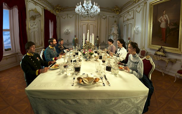 Dining scene in Schönbrunn Palace with people in period attire around an ornate table.