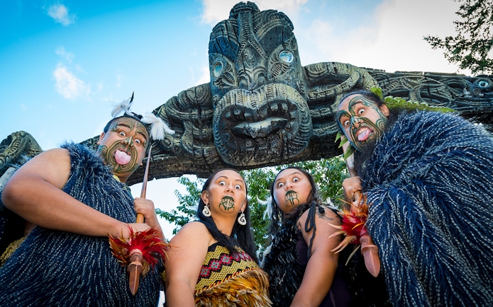 Mitai Maori performers in traditional attire under carved arch, New Zealand.