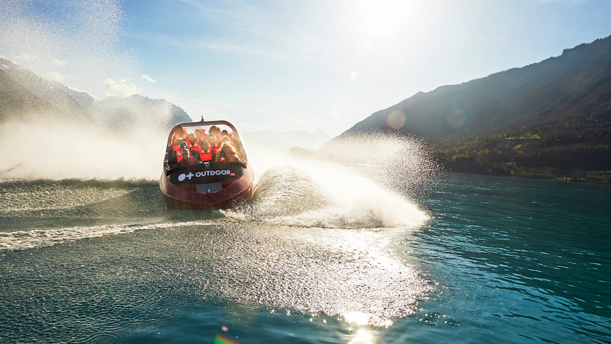 Jetboat speeding across turquoise waters of Lake Brienz, Interlaken, surrounded by lush mountains.