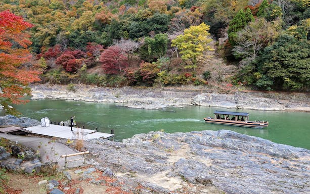 Boat on Hozugawa River in Kyoto with autumn foliage in the background.