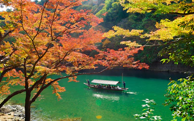 Boat on Hozugawa River in Kyoto surrounded by autumn foliage.