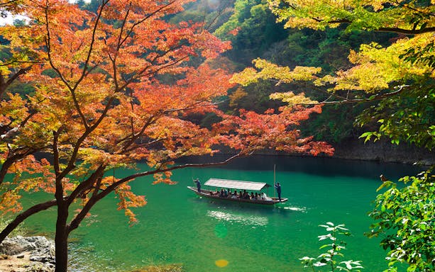 Boat on Hozugawa River in Kyoto surrounded by autumn foliage.
