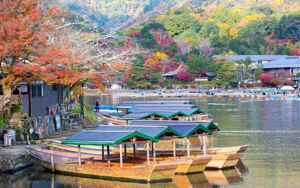 Traditional boats on Hozugawa River in Kyoto with autumn foliage in the background.